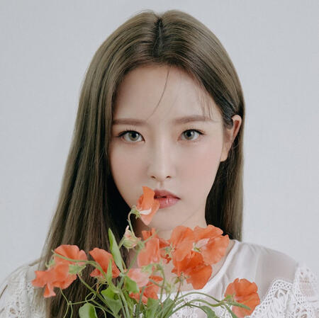 olivia hye from loona. she's staring straight at the camera and holding a bundle of orange lobelia flowers